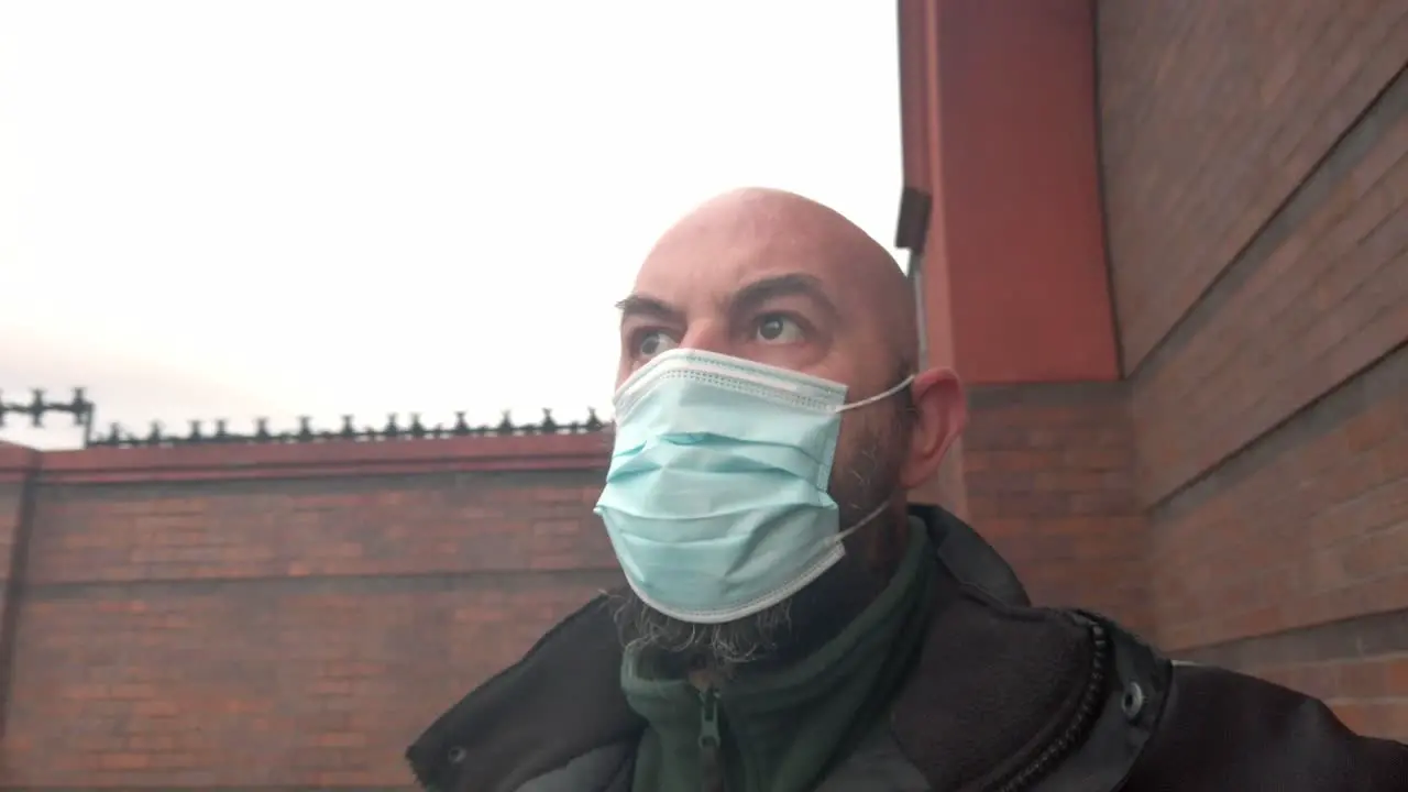 Male security guard wearing protective corona virus medical PPE mask right pan against brick wall