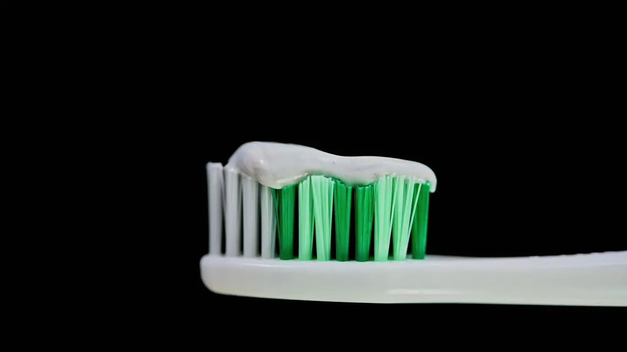 A zoom out of a toothbrush with white and green bristles loaded with toothpaste revealing a dark background