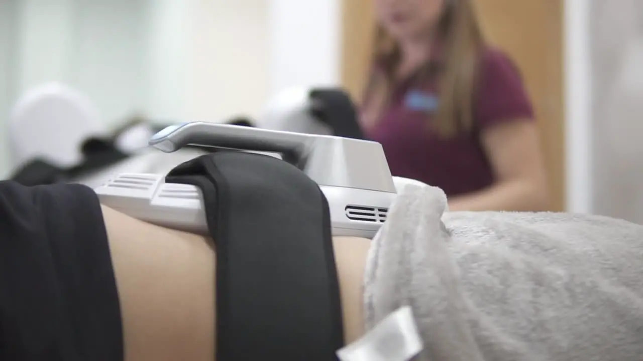 A young adult caucasian female client is using the innovative non-surgical sculpting procedure for toning her abdomen area while a blonde female cosmetologist supervises close up no face slow motion