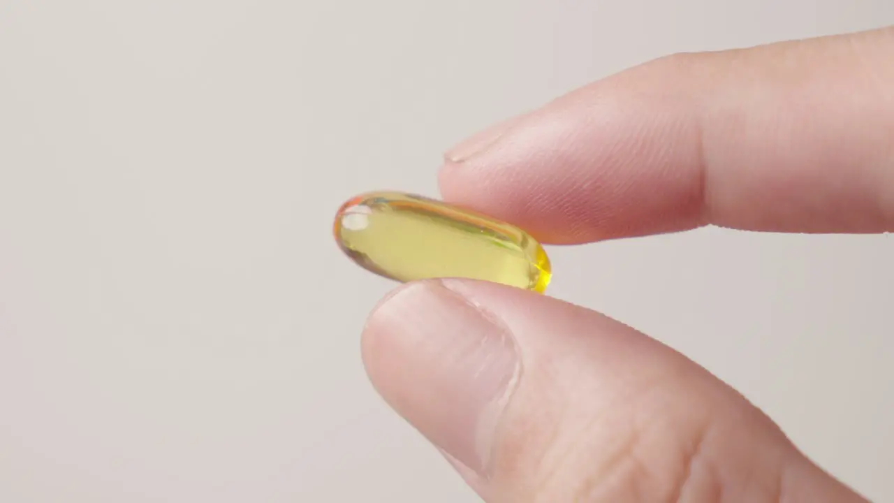 Hand holding fish oil supplement yellow pill