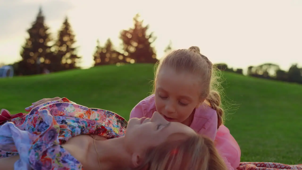 Girl kissing woman on green grass Mother and daughter playing in city park