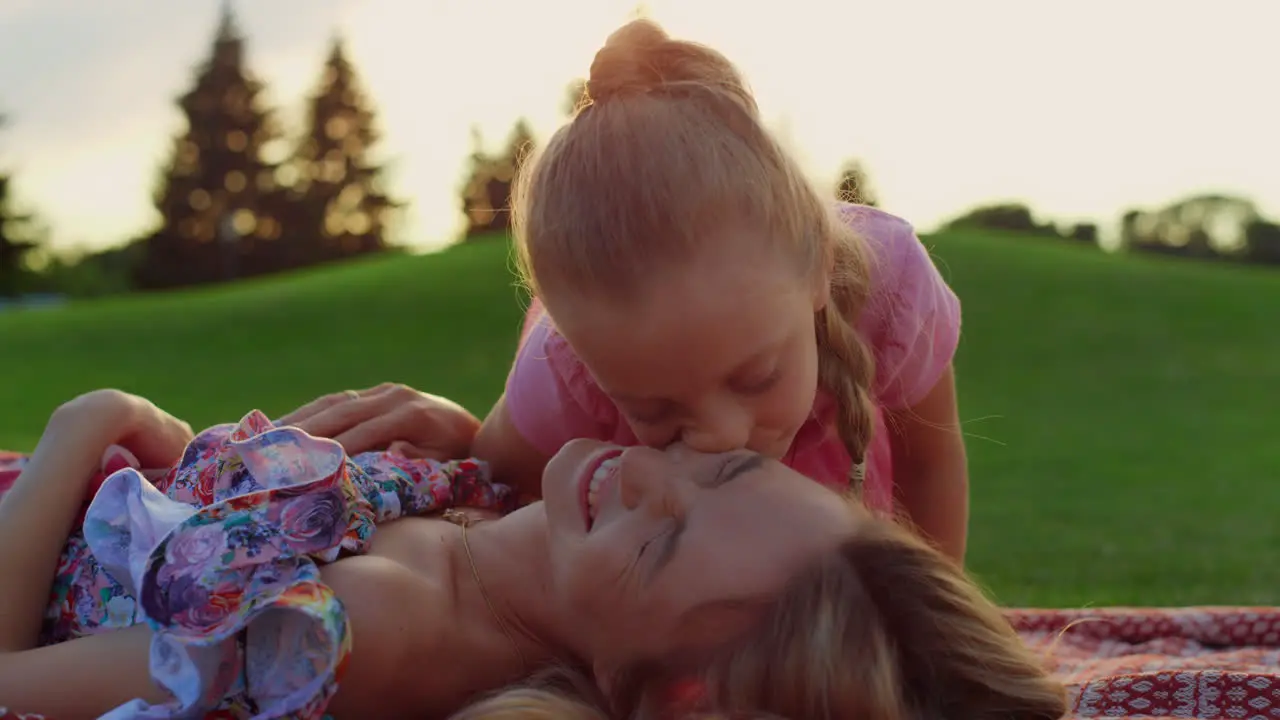 Woman laughing with girl at meadow Daughter kissing mother in city park