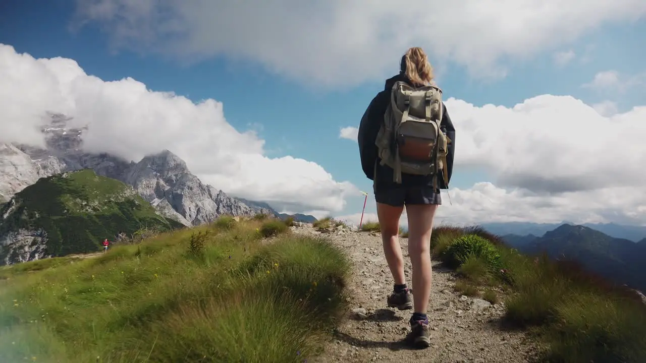 view from behind of a hiker tourist traveler woman with backpack trekking and walking on a mountain path with the dolomites in the background