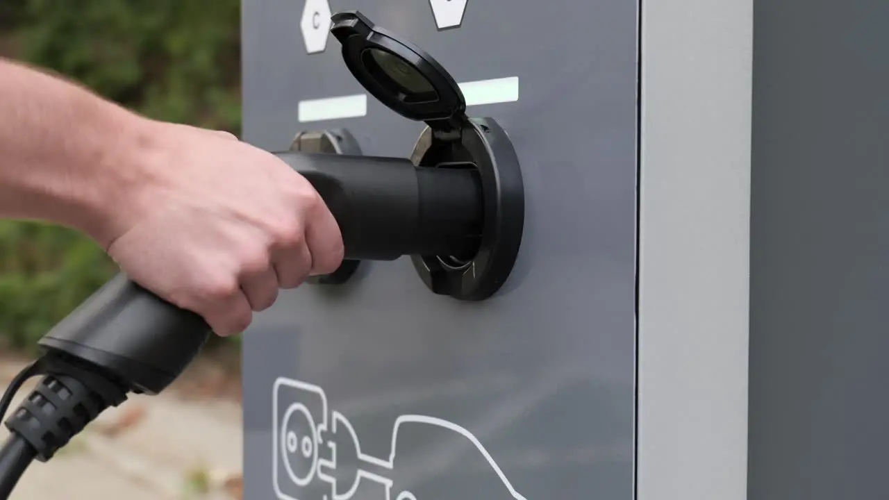 Close up on man plugging in electric car to outdoor charger station