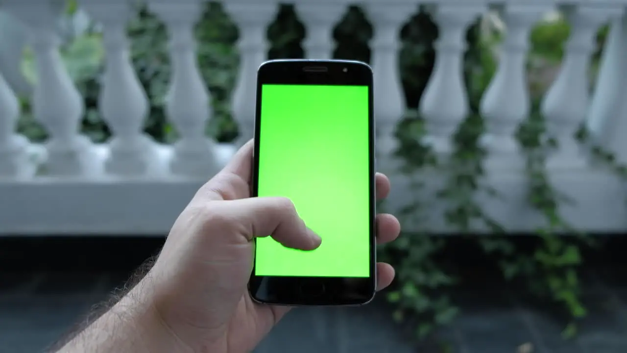 Close up shot of man hand scrolling with smartphone garden with plants on background