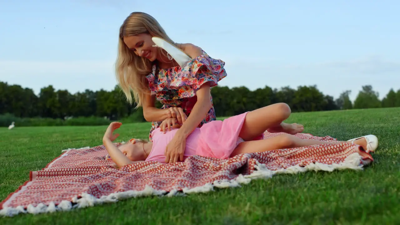 Woman fooling with daughter in city park Family enjoying sunset at meadow