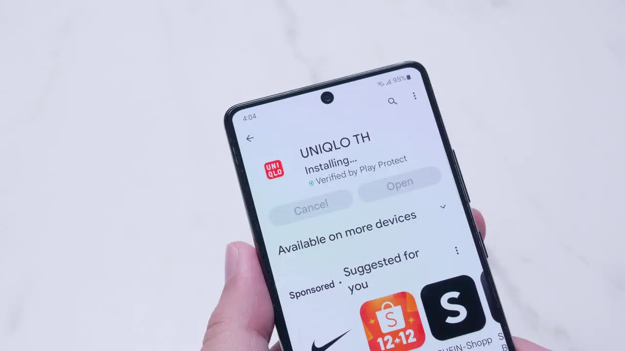 Hand holding a smartphone with installing UNIQLO application from Google play store