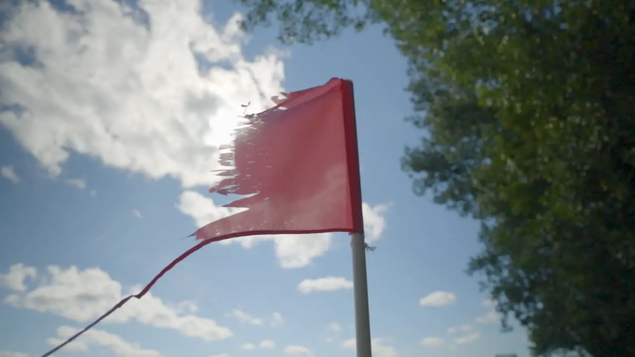 Old torn ratty red flag flowing in the wind on a sunny day