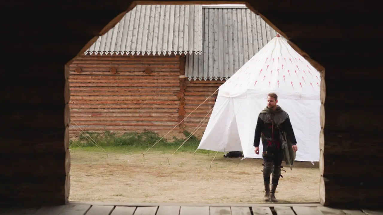 Armed man in cloak walks near gate looking at territory