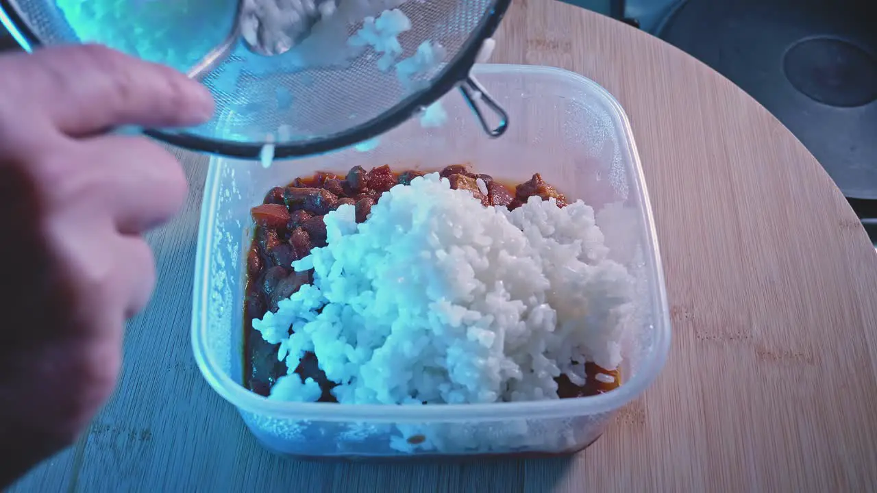 Adding Rice Into Food Container Filled With Cooked Spicy Chicken With Beans