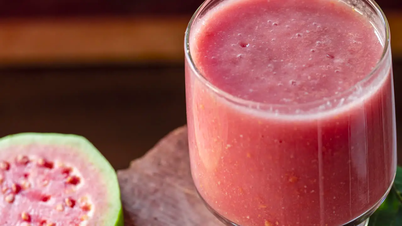 Glass of red guava juice and sliced guava slice on wooden background