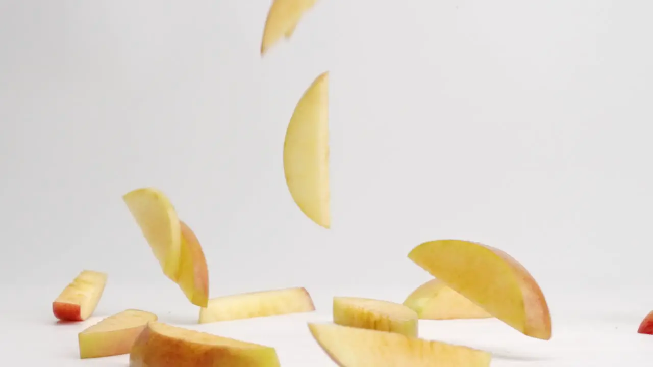 Sliced red and yellow fuji apple pieces falling onto white table top and bouncing into a pile in slow motion