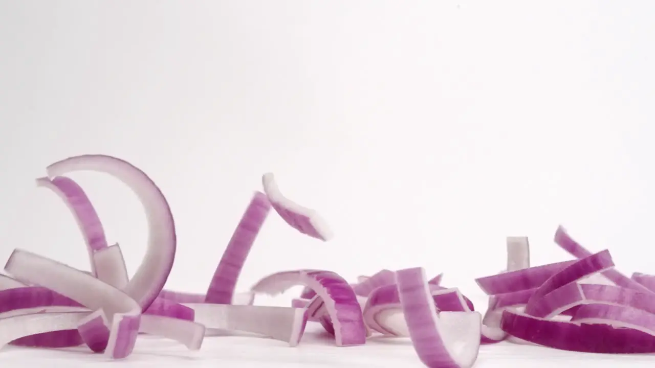 Red onion vegetable slices falling and bouncing into pile on white table top in slow motion