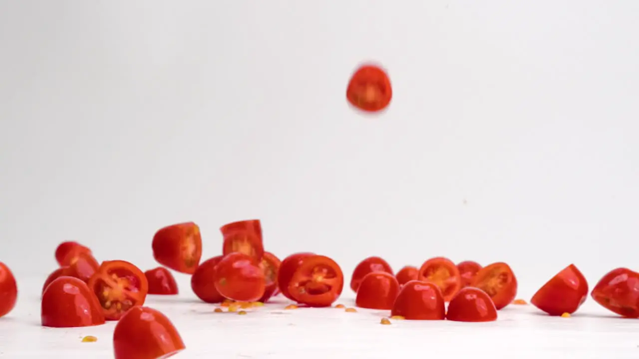 Fresh bright red halved cherry tomato fruits and vegetables landing down and bouncing on white table top in slow motion