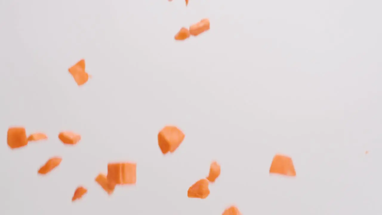 Cubed orange sweet potatoes raining down on white backdrop in slow motion