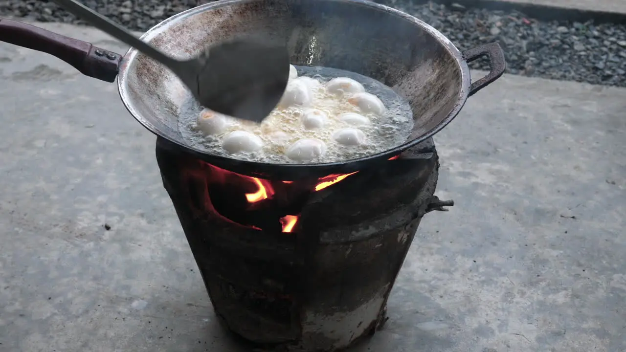 Motion shot cooking duck eggs outdoors in hot oil on Thai clay stove traditional street food