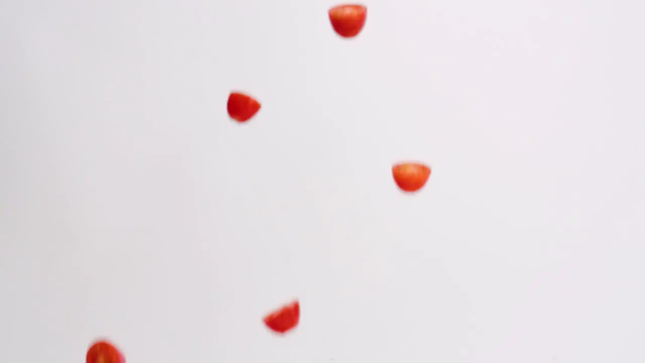 Fresh bright red halved cherry tomato fruits and vegetables raining down on white backdrop in slow motion