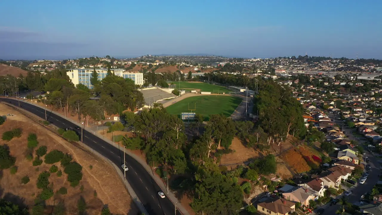 Crane up over a Residential Los Angeles Town with High School and Football Field ontop of Hill on Bright Blue Day California USA