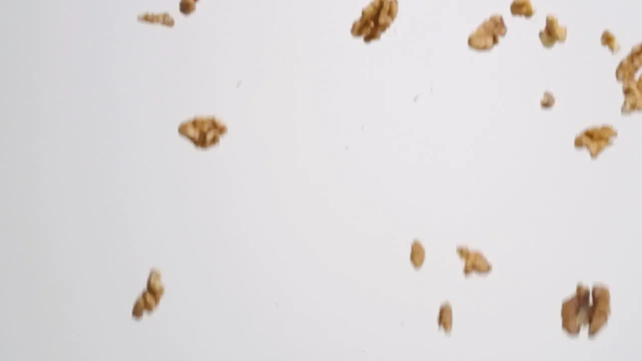 Fresh raw brown walnut pieces raining down on white backdrop in slow motion