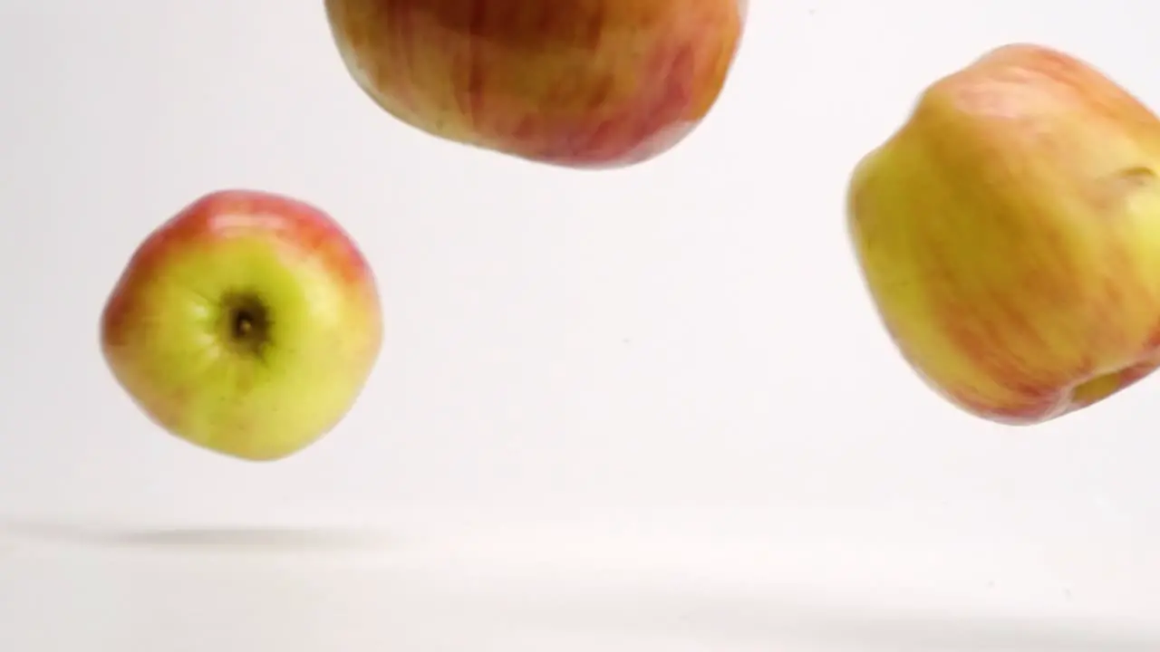 Whole red and yellow fuji apples falling onto white table top and bouncing and rolling around in slow motion