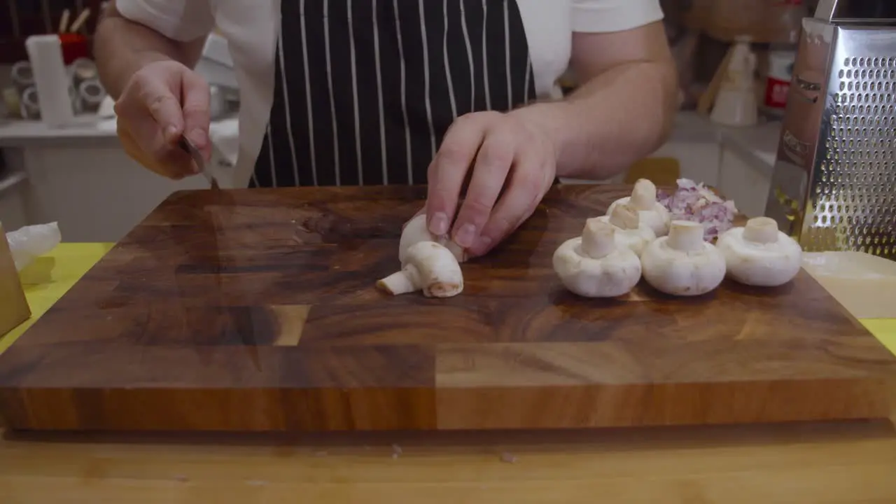 Chef cuts white mushrooms on wooden cut board in the kitchen