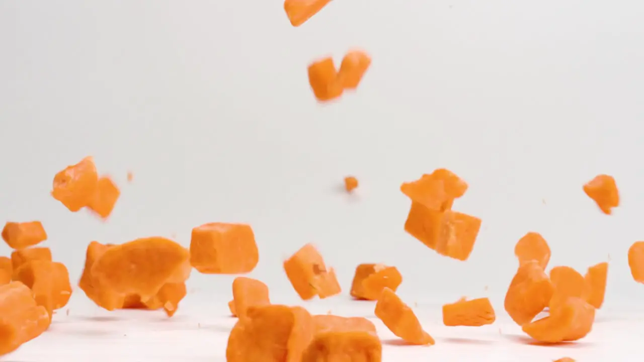 Bright orange cubed sweet potato pieces falling and bouncing onto white table top in slow motion