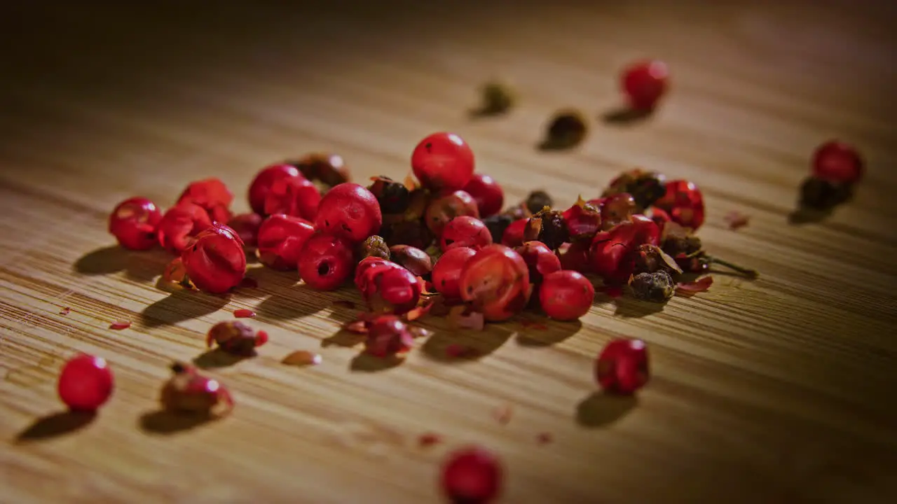 A pile of pink peppercorn on a wooden surface with dramatic lighting camera orbiting