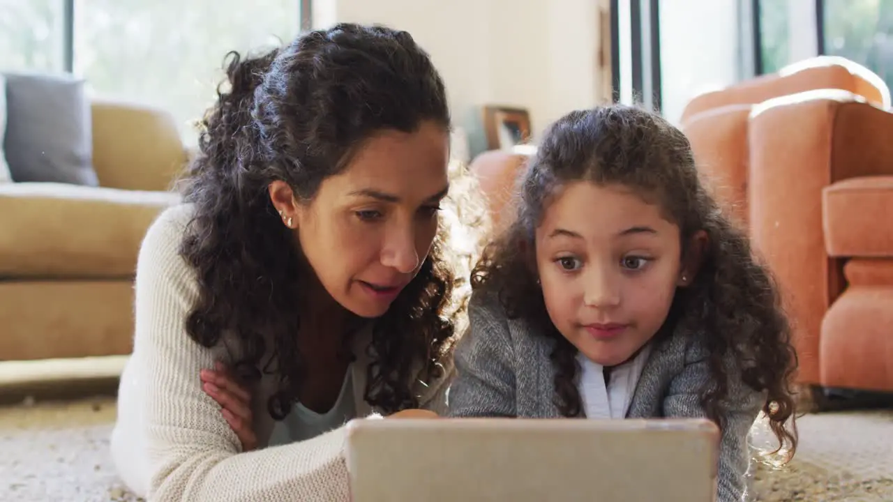 Happy mixed race mother and daughter laying on the floor having fun and using tablet