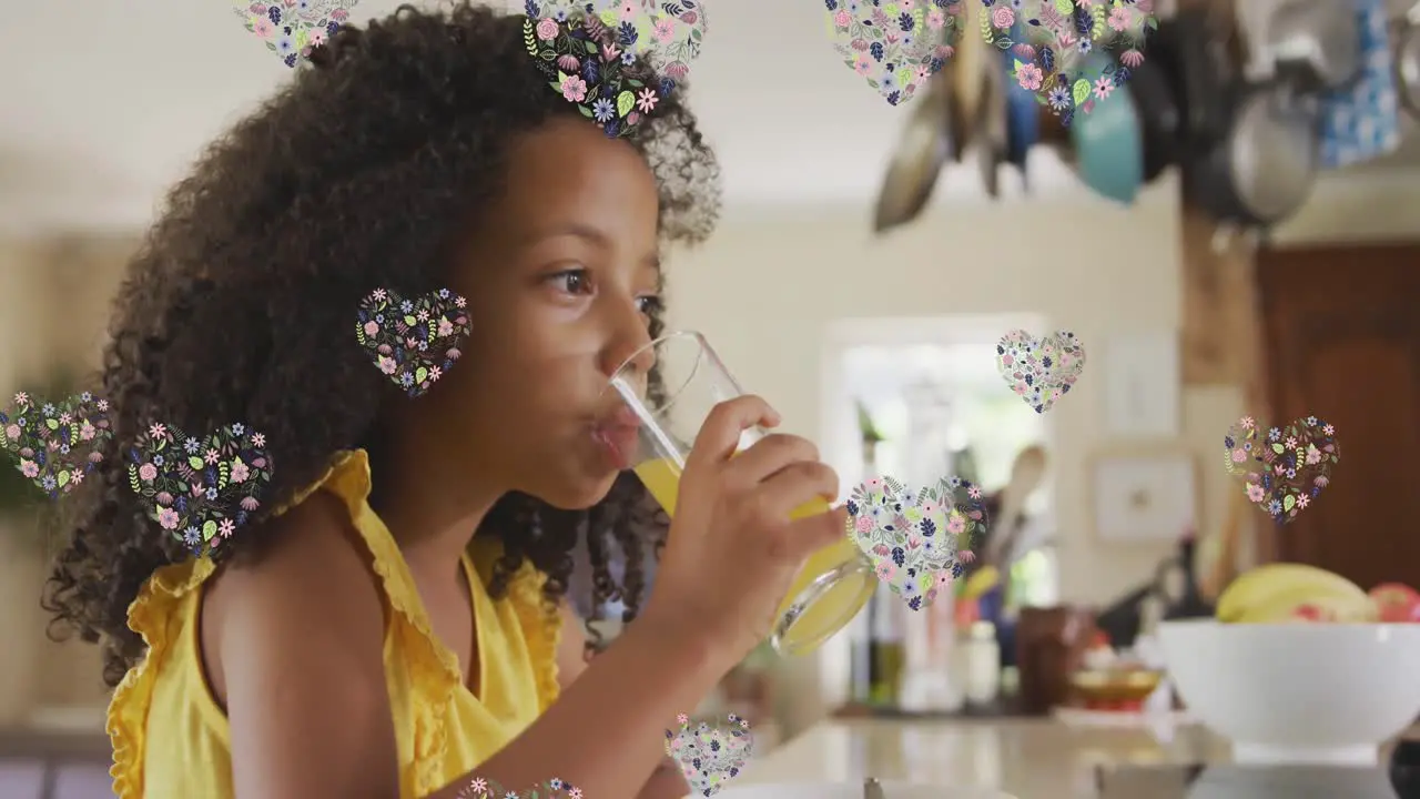 Animation of flower hearts over african american girl drinking juice at home