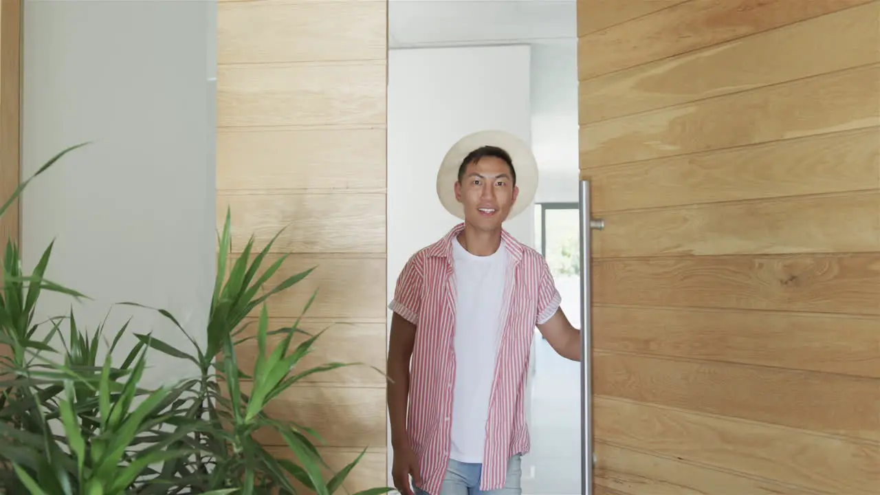 Young Asian man stands smiling at the entrance of a modern home