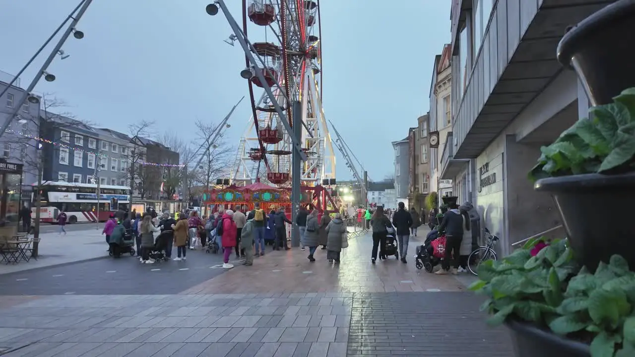 Street in Cork city evening in winter people gathered around lit Ferris wheel in Ireland