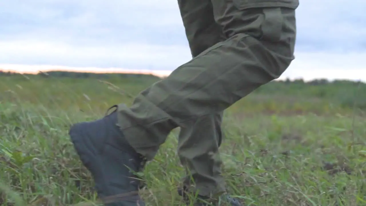 Low angle shot of person walking on green grass field outdoors with military protection outfit