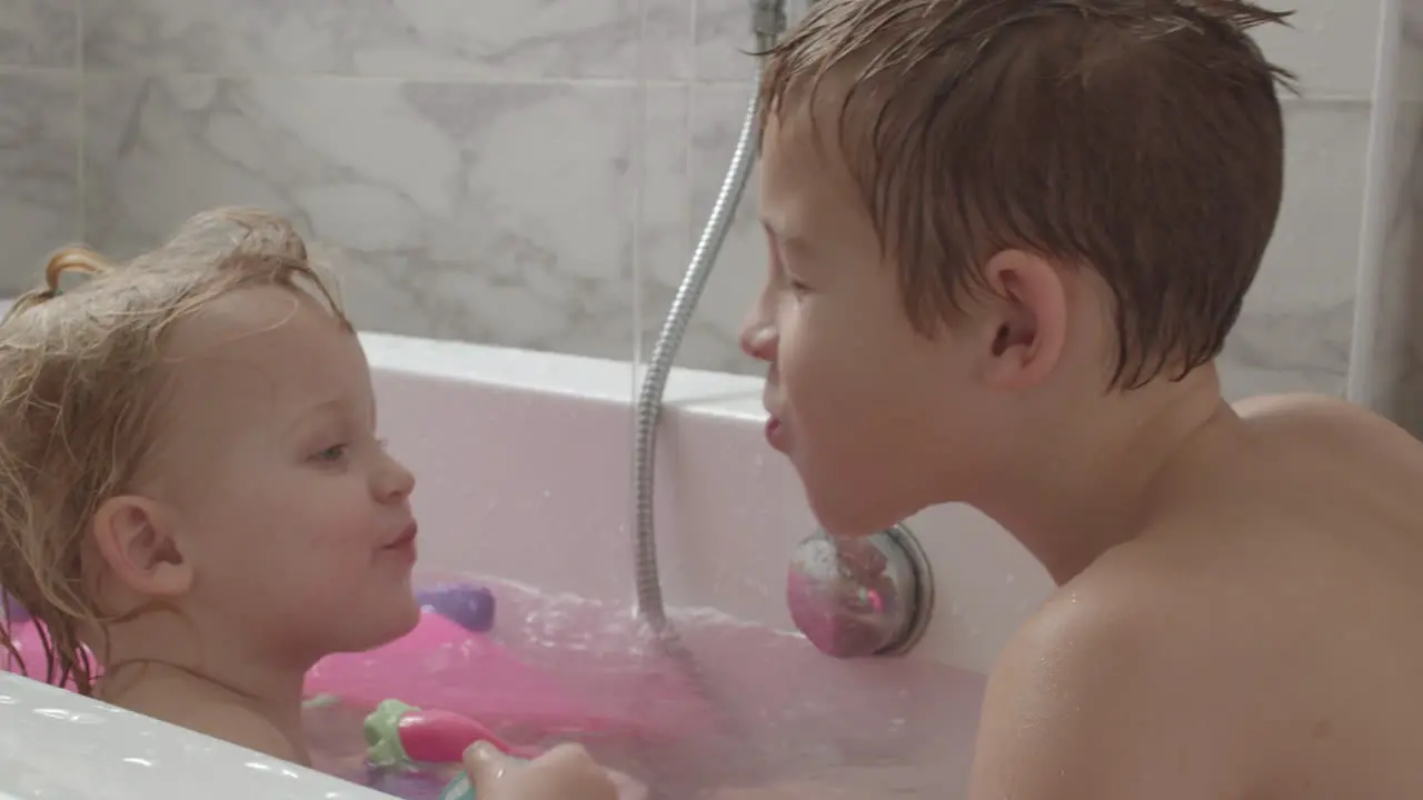 A baby girl and her brother playing in the bath