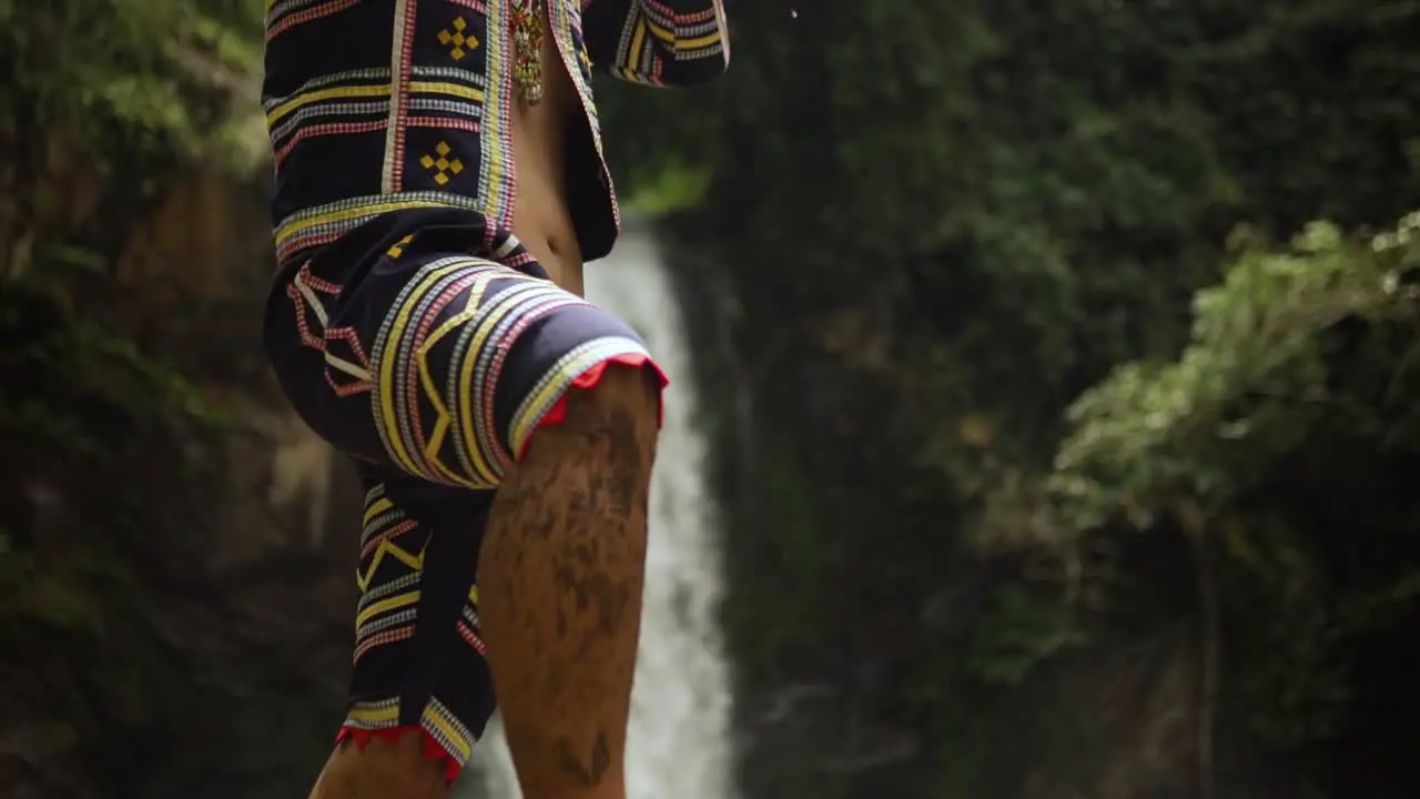 Indigenous person playing Kubing tribal instrument behind is a waterfall while standing