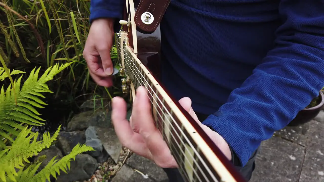 Practicing playing rock music on electric guitar in the garden near the pond