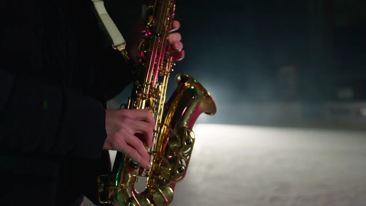 Slowmotion of saxophone player playing a song on a snow covered winter stadium with ice skaters in background