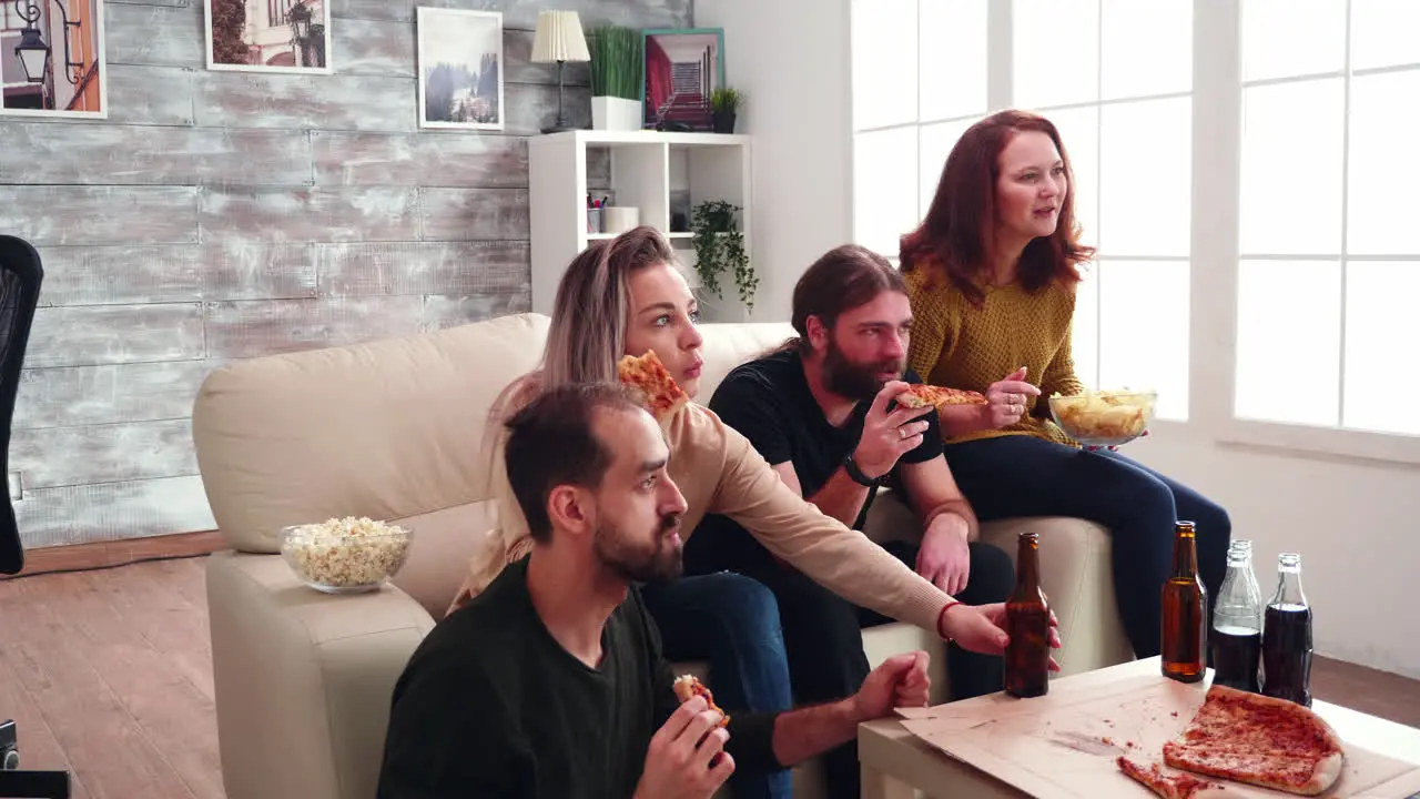 Group of close friends with mouth full of pizza celebrating victory