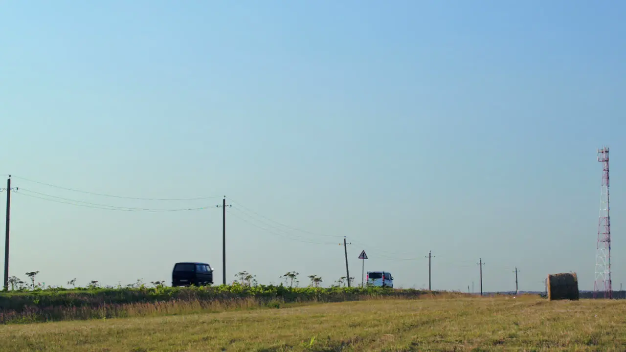 Cars going by field with hay roll in countryside