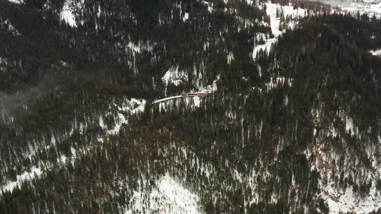 high aerial shot over forest with a viaduct in the center while a red train is passing by