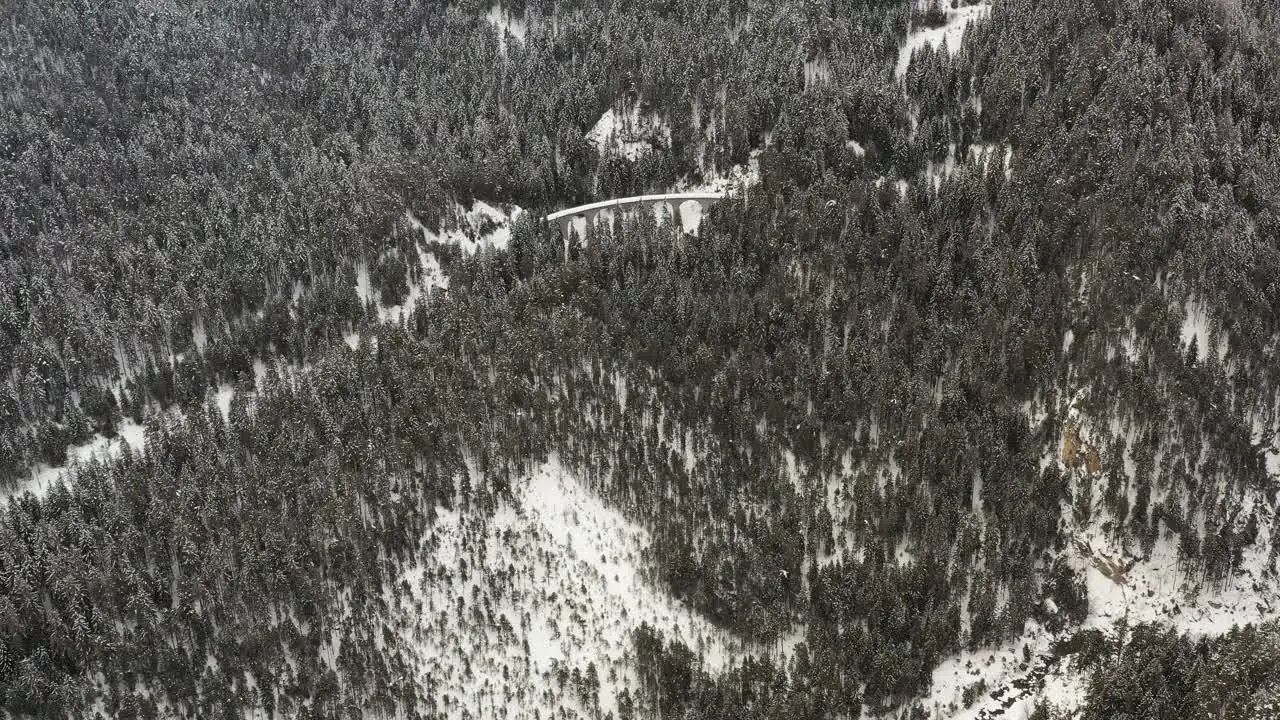 Flying over snowy mountain forest towards a viaduct