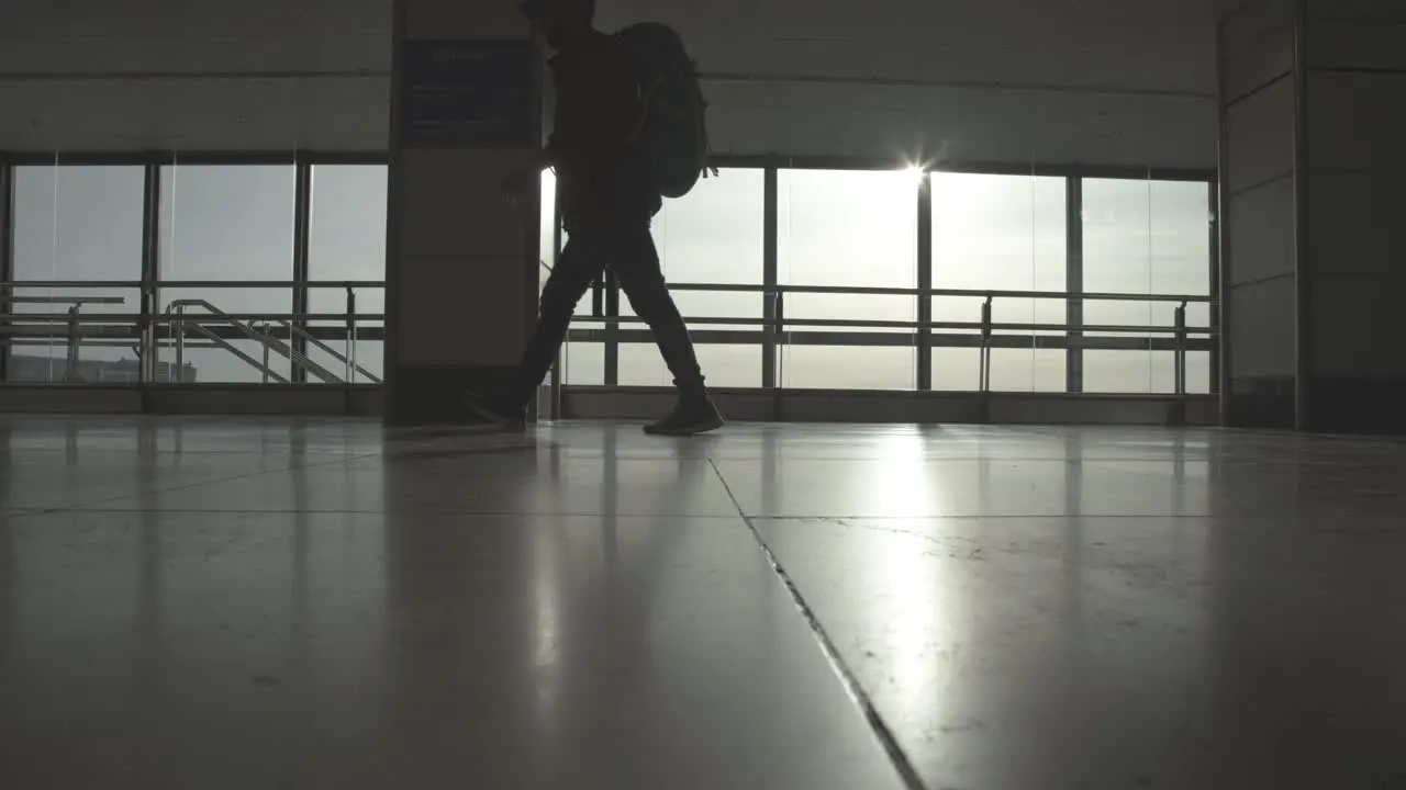 Traveler walking through airport hall sun flare static shot low angle