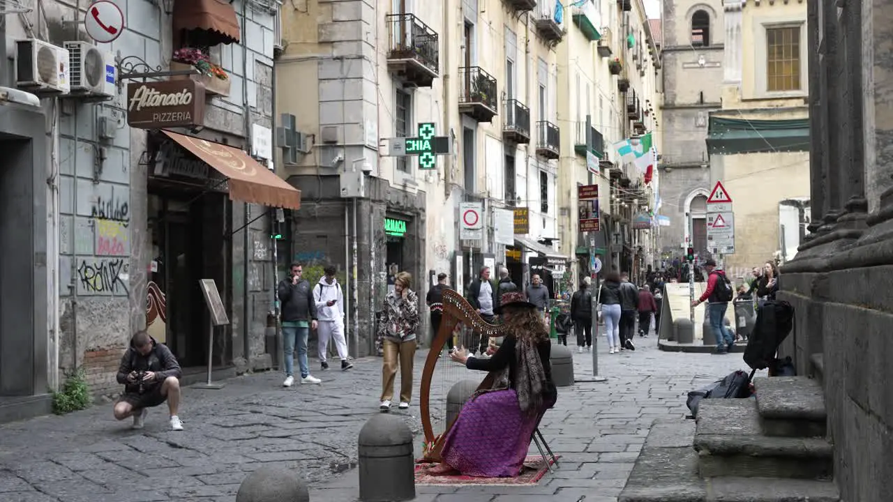 A slow motion shot of a musician playing music on a harp on a busy city street in Naples Italy