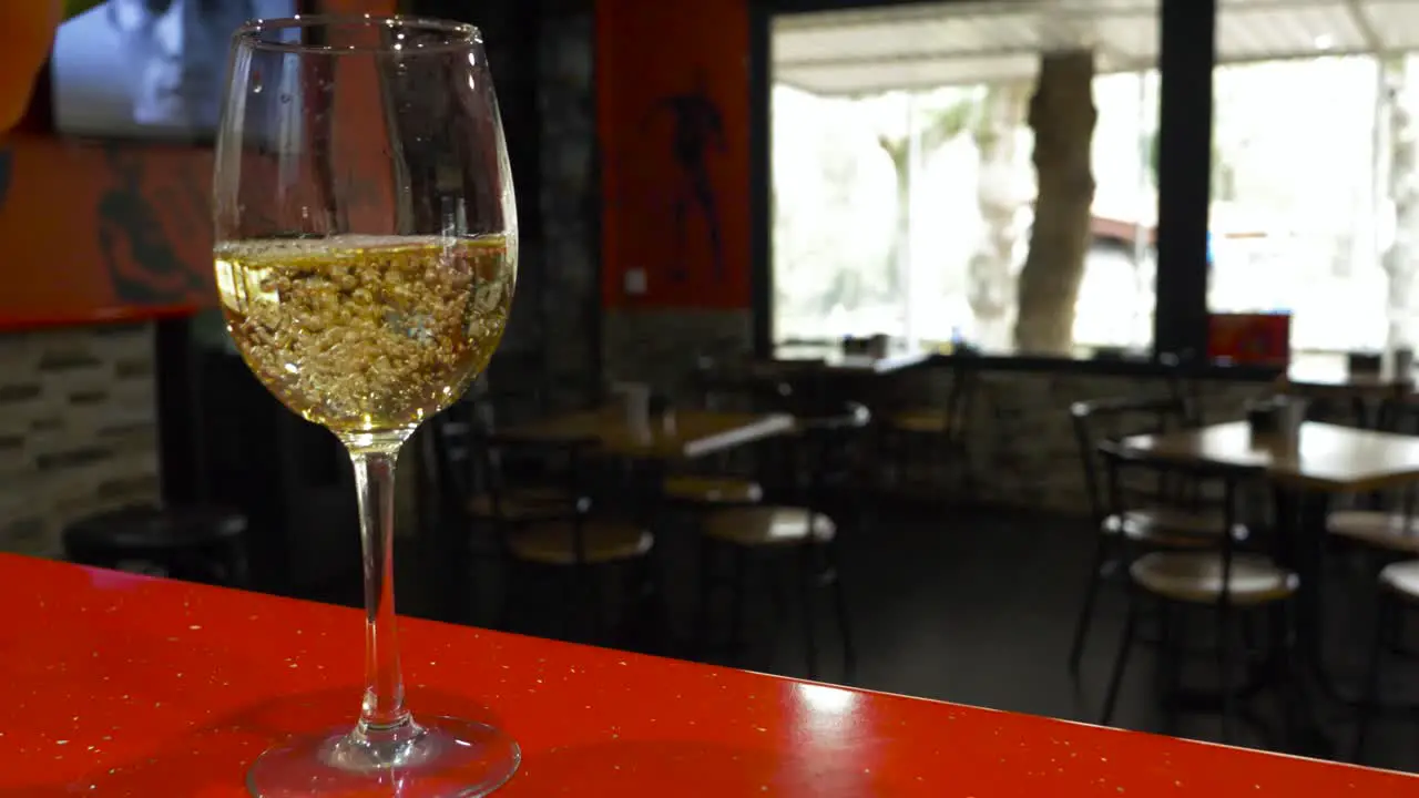 Empty glass is filled with white win as TV plays in background of empty restaurant