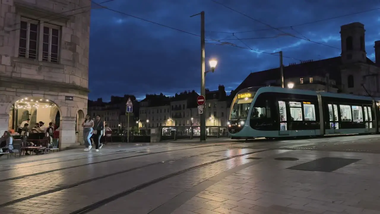 Night street with tram crossing over bridge and people walking in Besancon France with streetlights and cafe