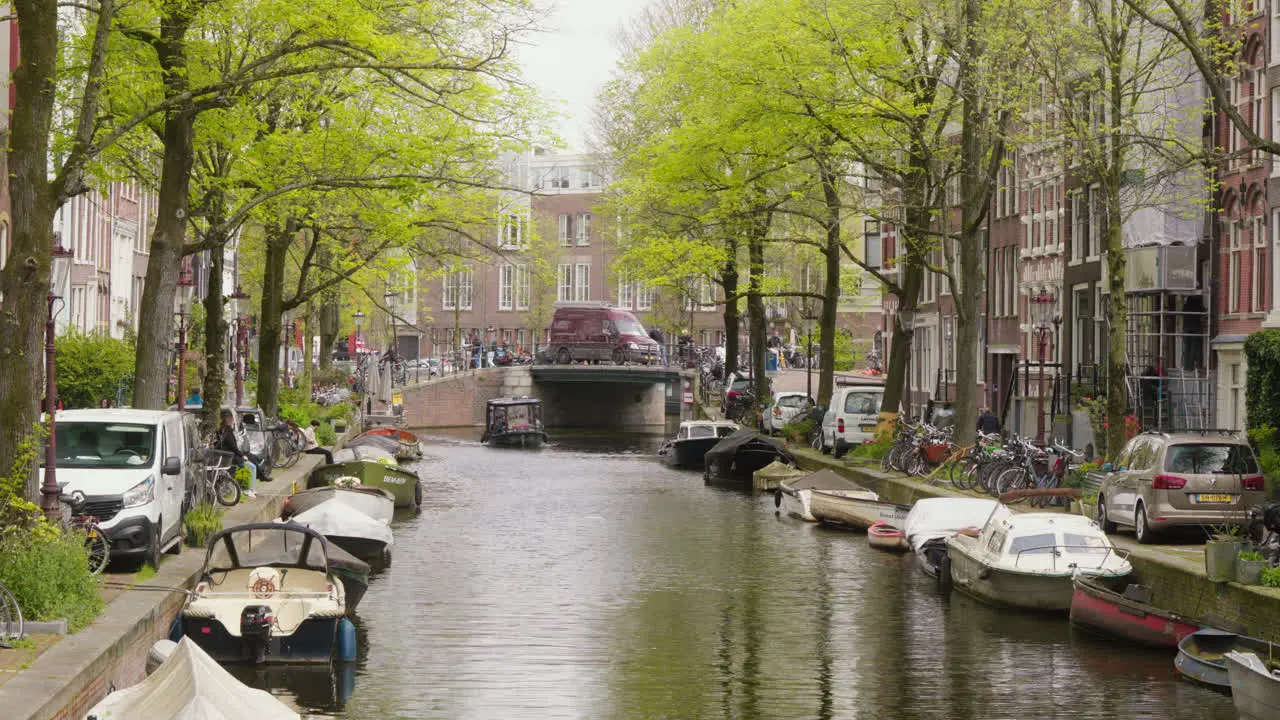 A picturesque view of an Amsterdam canal bordered by lush green trees with a boat traversing the water