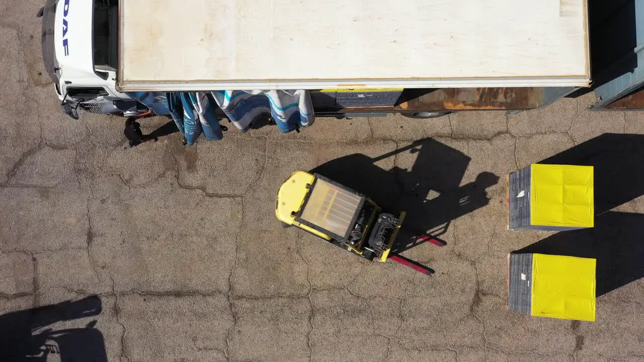 forklift loading product pallets into shipping truck bird's eye view