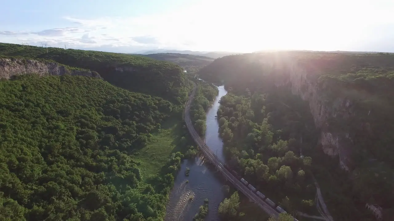 Passing a train on a bridge over a river at sunset surrounded by forest aerial