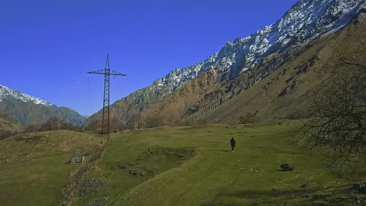 Lonely walking man in mountains with poncho and stick high voltage line trees snowy mountain aerial view