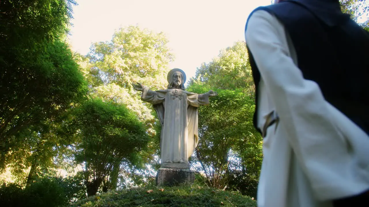 Amazing gimbal shot in a scene with a monk praying at a jesus statue in the forest