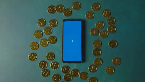 Overhead Studio Shot Of Gold Coins Surrounding Blue Screen Mobile Phone To Celebrate St Patricks Day